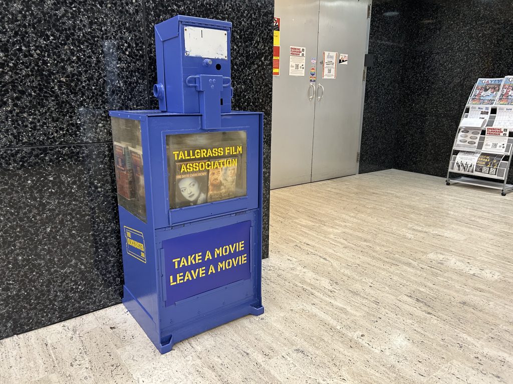 Blue bin with words Free Blockbuster and Leave a Movie Take A movie stenciled on it in yellow.