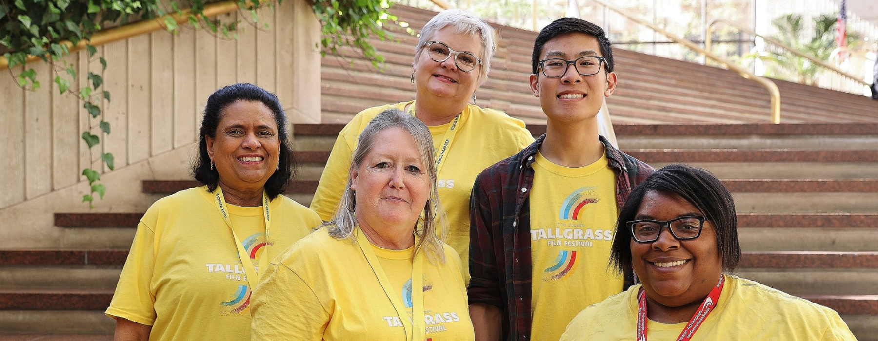 5 volunteers stand in front of a set of stairs wearing bright yellow shirts